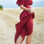 woman in red polka-dot dress standing in the middle of grass field during daytime